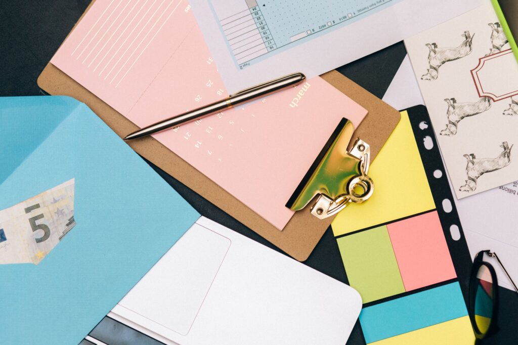 Neatly arranged desk supplies with clipboard, euro bill, and colorful notes.