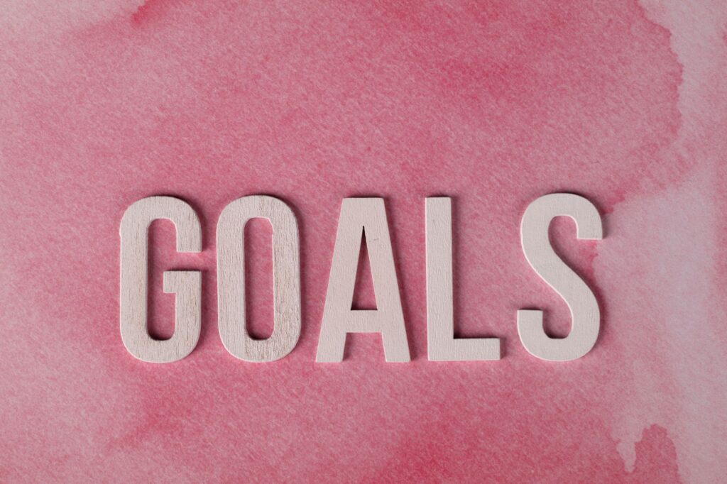 Motivational word 'GOALS' on a pink watercolor background for inspiration.