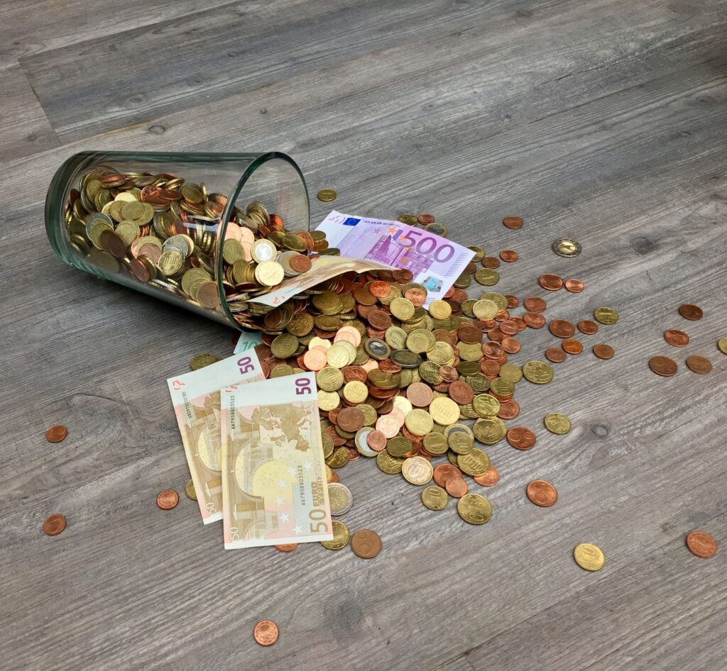Glass jar filled with coins and cash on a wooden table