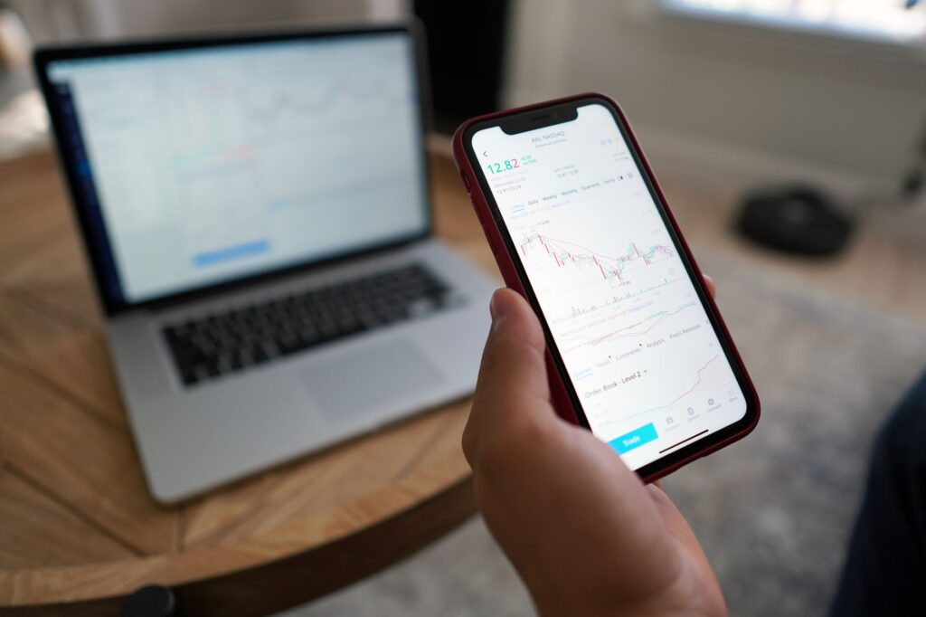 A person trading stocks on a smartphone and laptop. Ideal for finance themes.