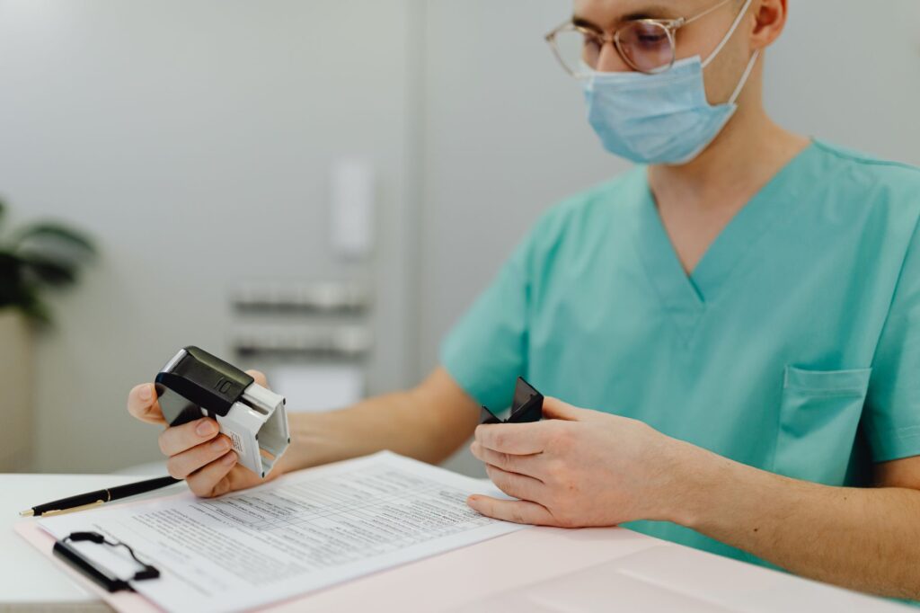 Healthcare worker in scrubs reviewing patient files with a stamp and clipboard.