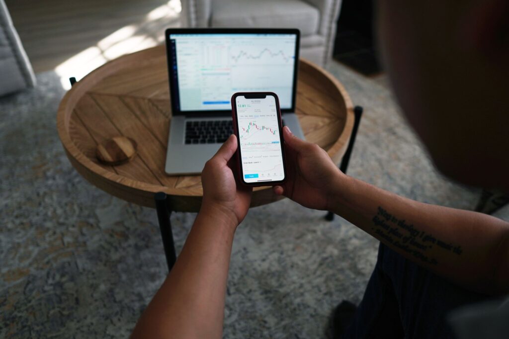 Person checking an investment app on their phone next to a laptop